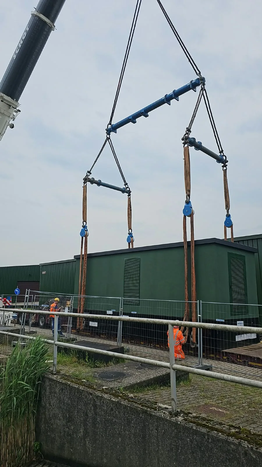 Kraan die een prefab stationsgebouw plaatst binnen een afgezette werf